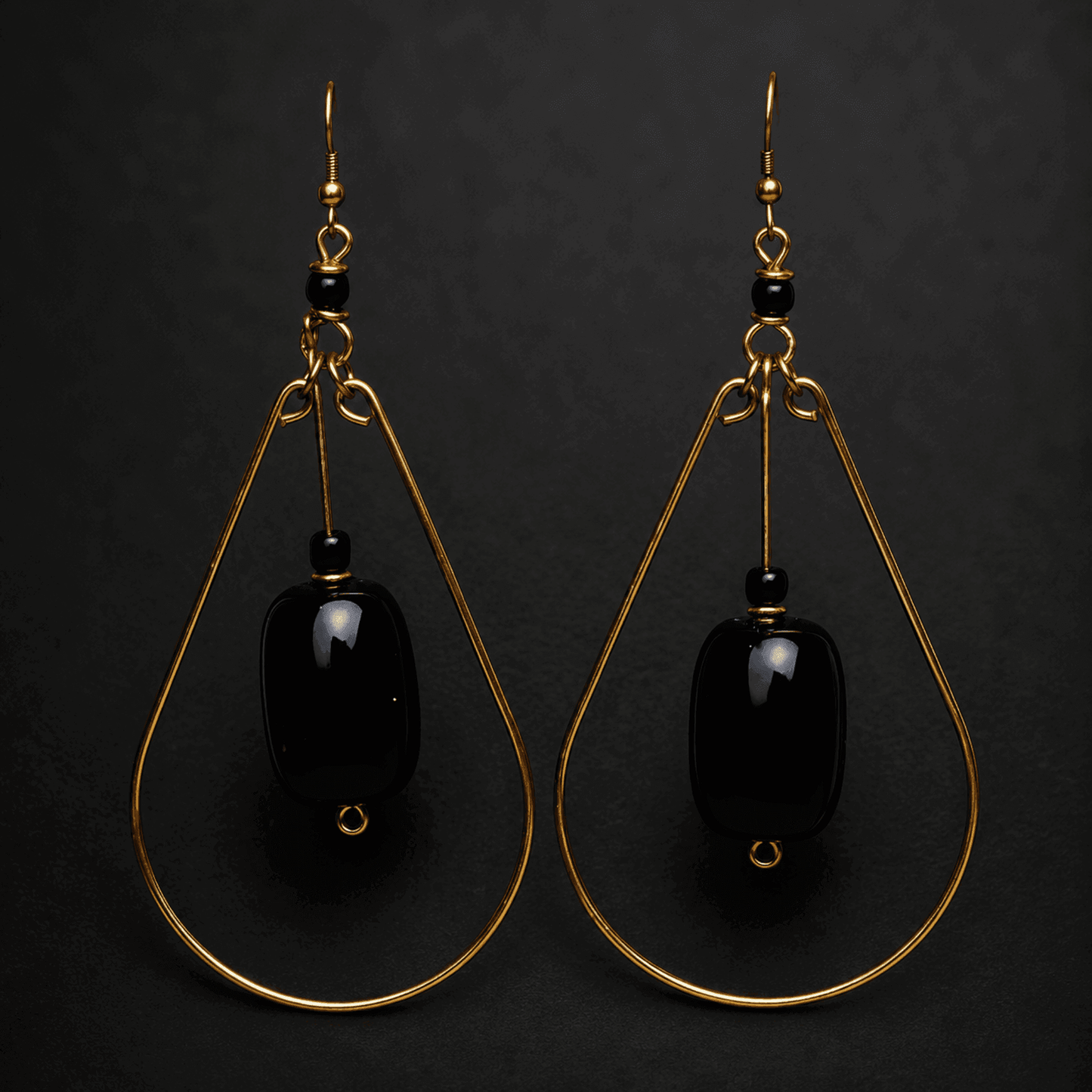 A pair of gold and black teardrop earrings on a black background.