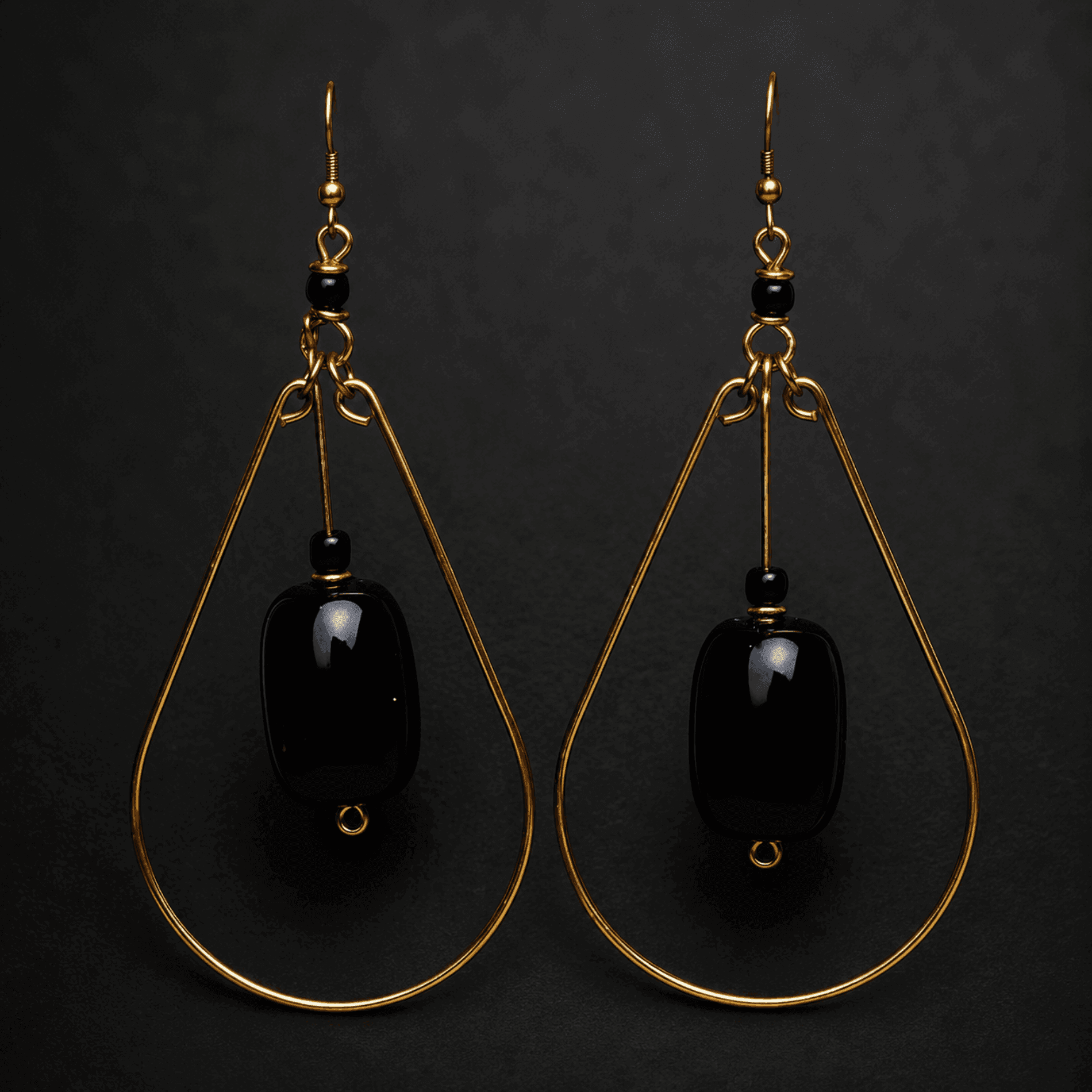 A pair of gold and black teardrop earrings on a black background.