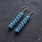 Blue beaded earrings on a gray fabric background