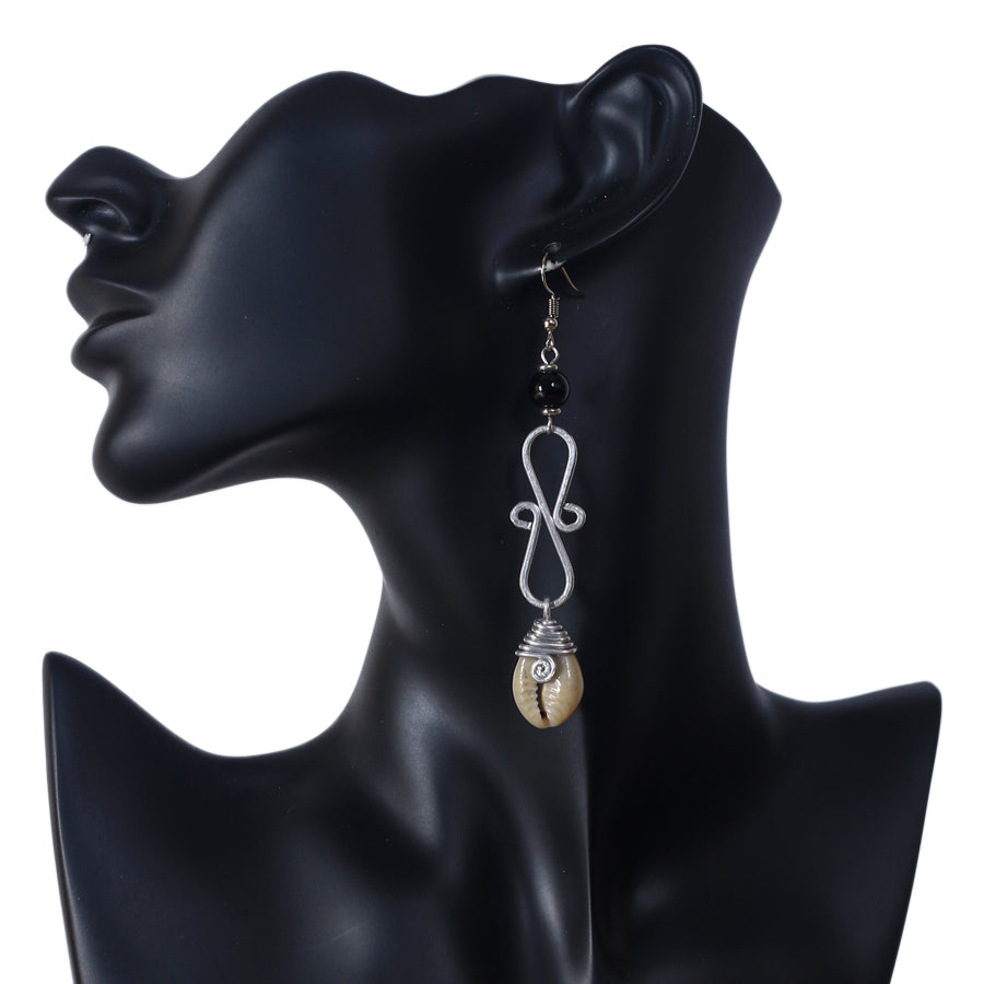 Long silver-plated dangle earrings featuring a black bead, a wire scrollwork design, and a wire-wrapped cowrie shell at the bottom.