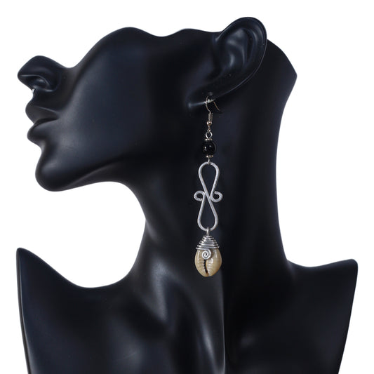 Long silver-plated dangle earrings featuring a black bead, a wire scrollwork design, and a wire-wrapped cowrie shell at the bottom.