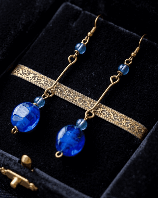 Gold earrings with blue beads on a black velvet background