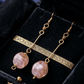 Long pair of earrings with pink beads and gold plated brass on a black velvet background