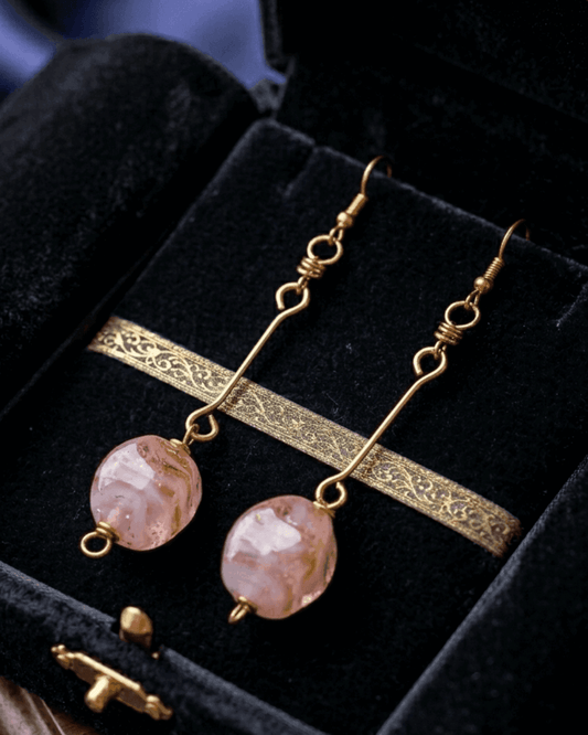 Long pair of earrings with pink beads and gold plated brass on a black velvet background