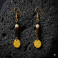 A pair of earrings handmade with porcupine quill and gold plated brass on a black lava textured background.
