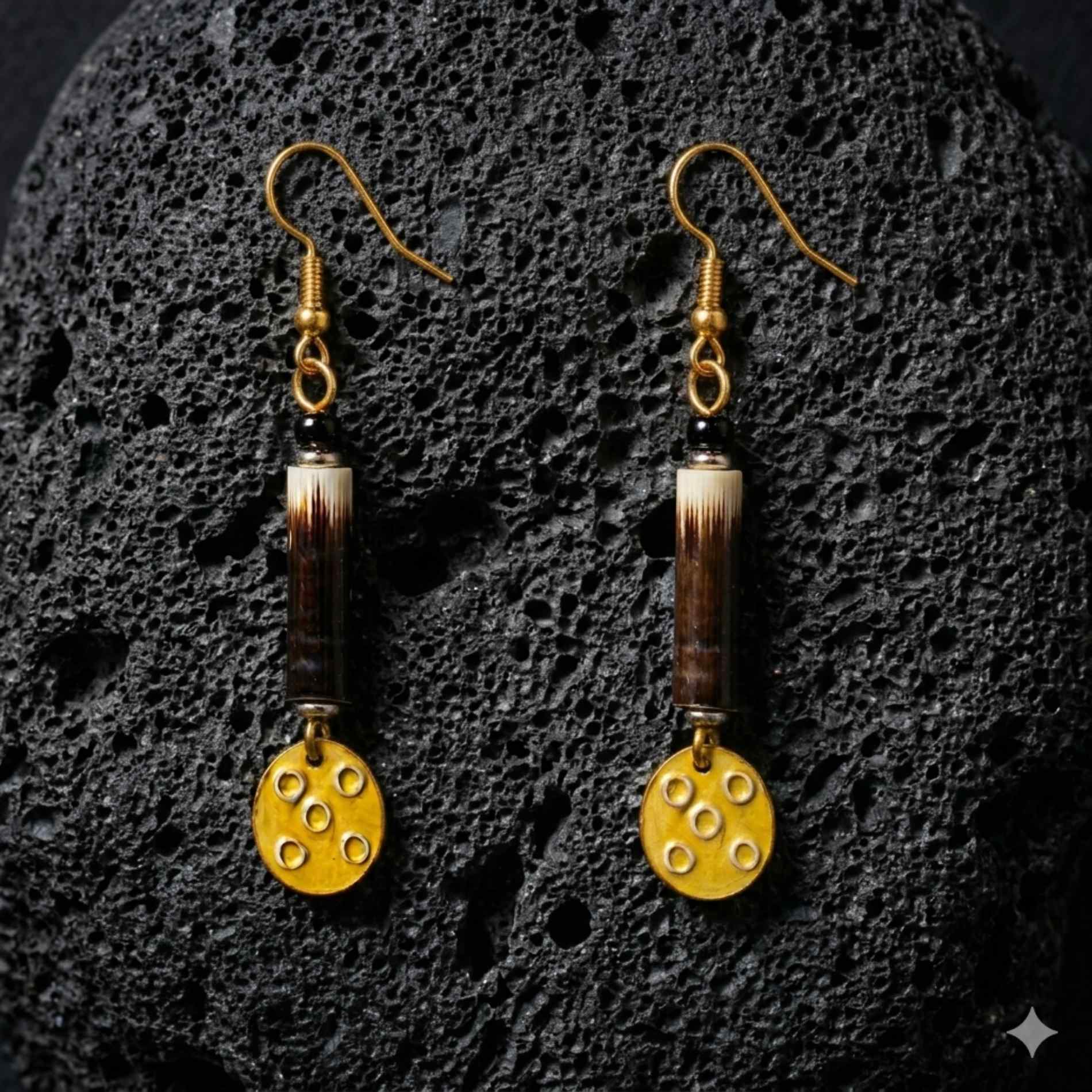 A pair of earrings handmade with porcupine quill and gold plated brass on a black lava textured background.