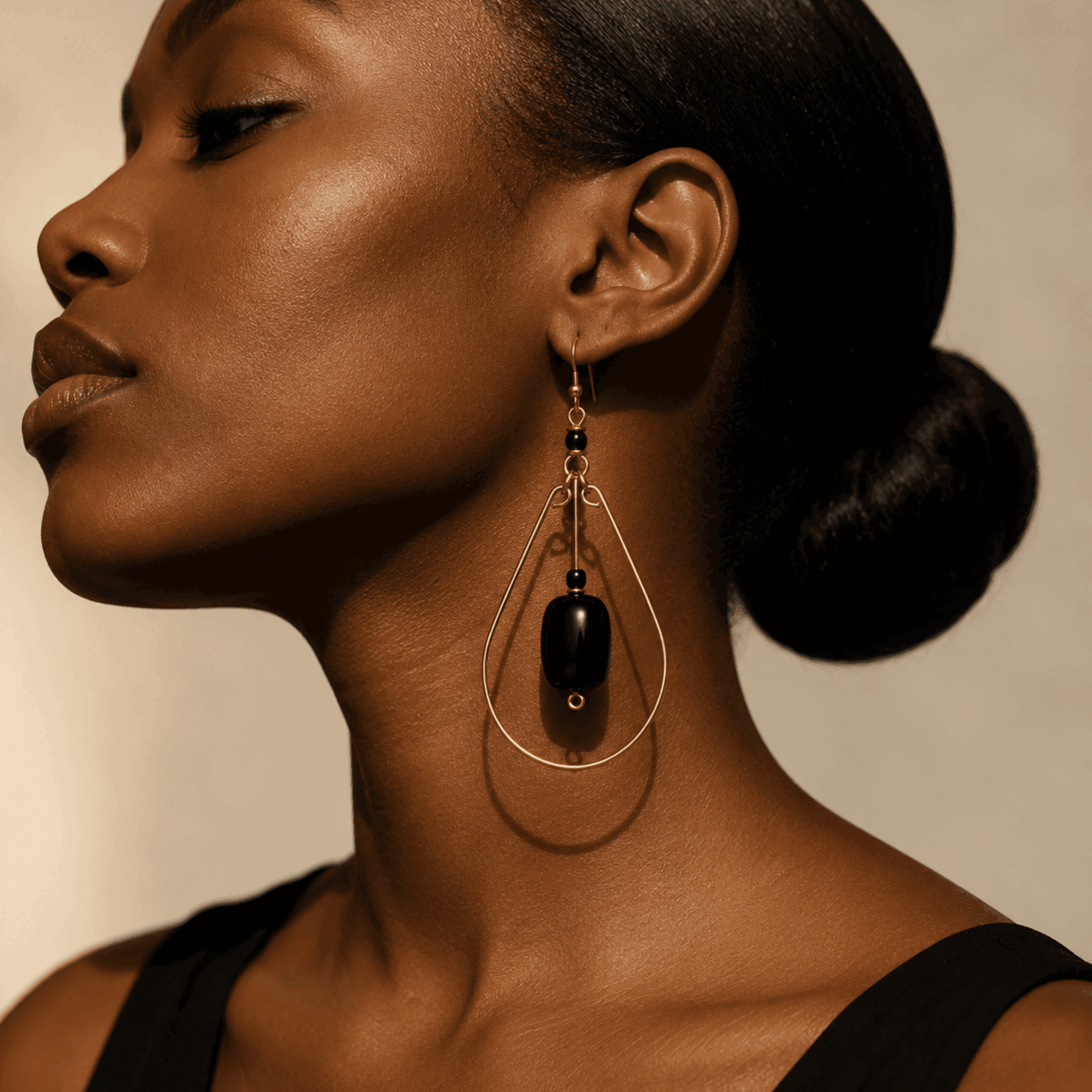 Close-up of a woman wearing teardrop hoop earrings. The hoop is made of gold. The earrings have a black bead in the middle.