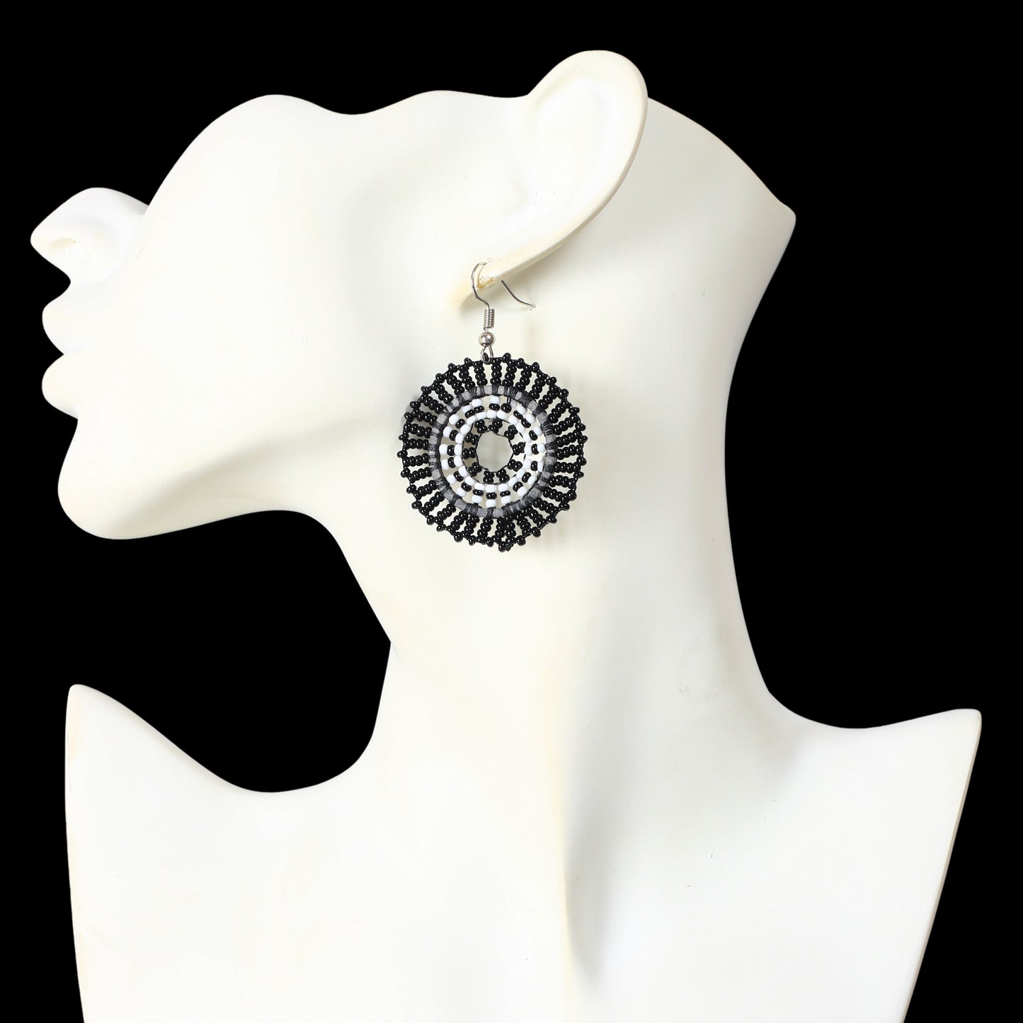 A pair of hand-woven black and white, beaded disc earrings in a concentric circle pattern.