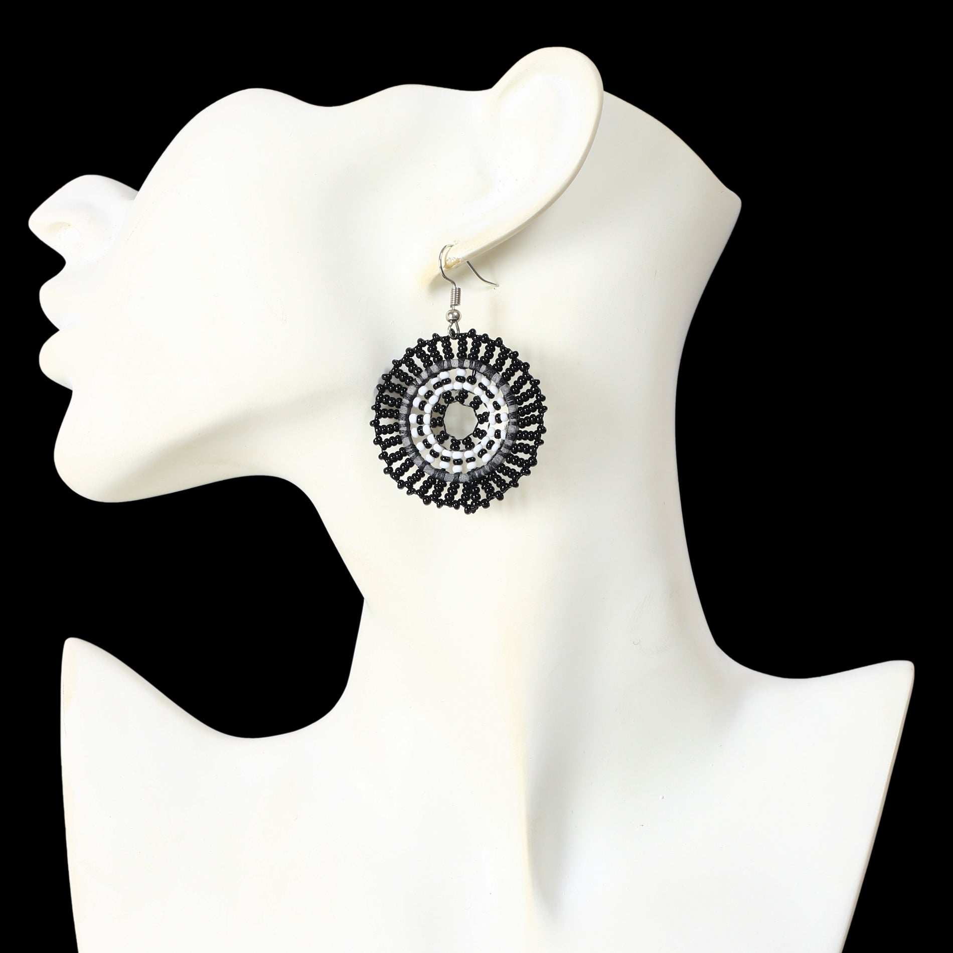 A pair of hand-woven black and white, beaded disc earrings in a concentric circle pattern.