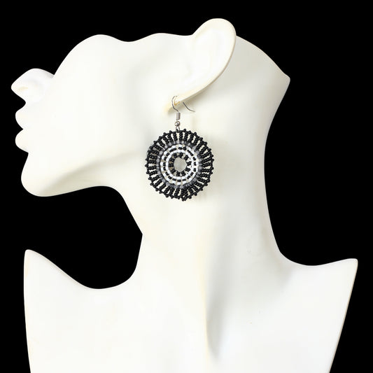 A pair of hand-woven black and white, beaded disc earrings in a concentric circle pattern.