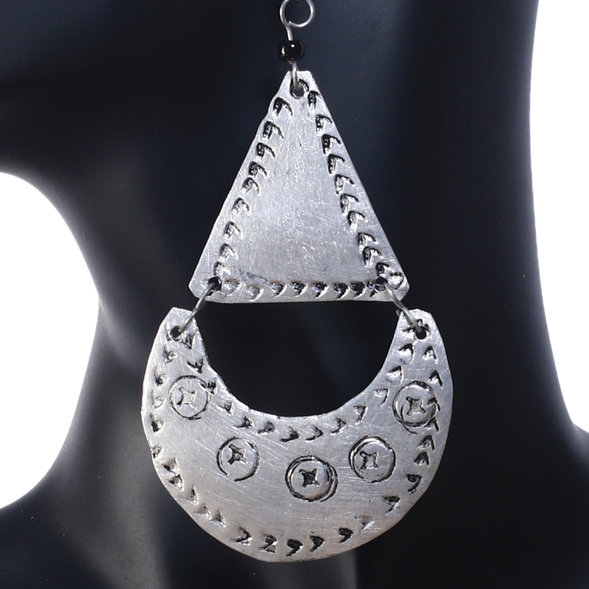 An upclose photo of a pair of large, silver-plated geometric earrings featuring an etched triangle and a stamped crescent drop.