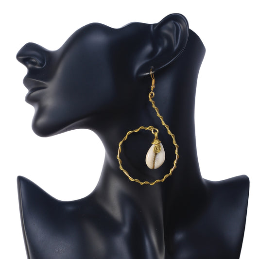 A pair of large, gold-plated spiral hoop earrings with a wavy texture, holding a wire-wrapped natural cowrie shell in the center.