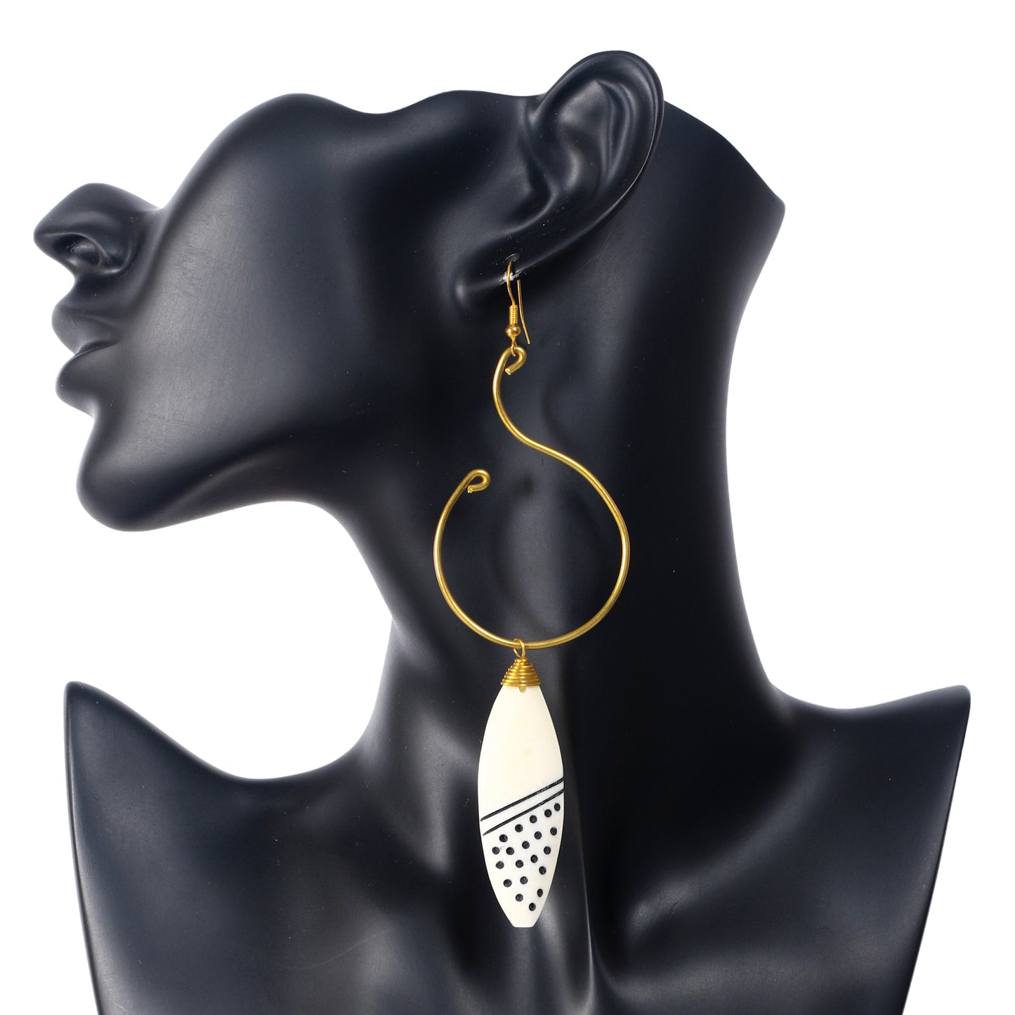 A pair of large, artistic gold wire hoop earrings with a hand-carved camel bone pendant with an etched geometric dot and line pattern.