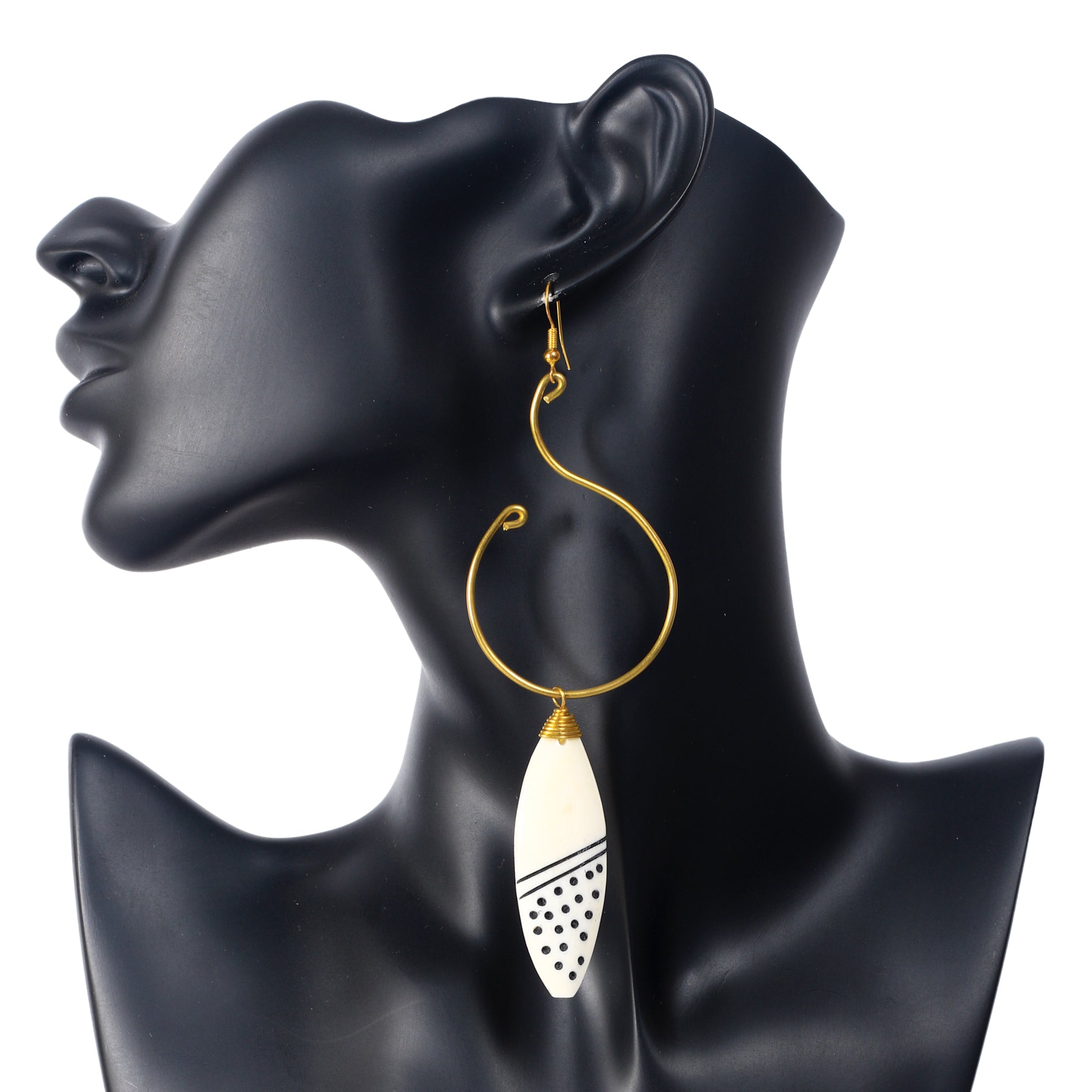 A pair of large, artistic gold wire hoop earrings with a hand-carved camel bone pendant with an etched geometric dot and line pattern.