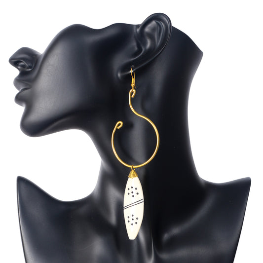 A pair of large, artistic gold wire hoop earrings with a hand-carved camel bone pendant with an etched dot pattern.