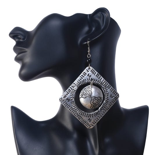 A pair of large, square, etched silver-plated earrings with a textured, free-moving disc in the center.