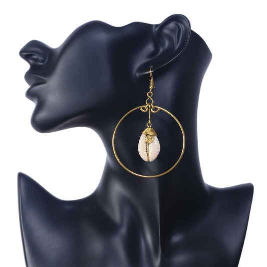 A pair of large, gold-plated hoop earrings with a single, wire-wrapped natural cowrie shell suspended in the center.
