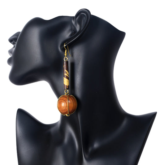 A pair of long, dangle earrings with a two-tone bamboo cylinder and a large wooden sphere in a gold wire cage.