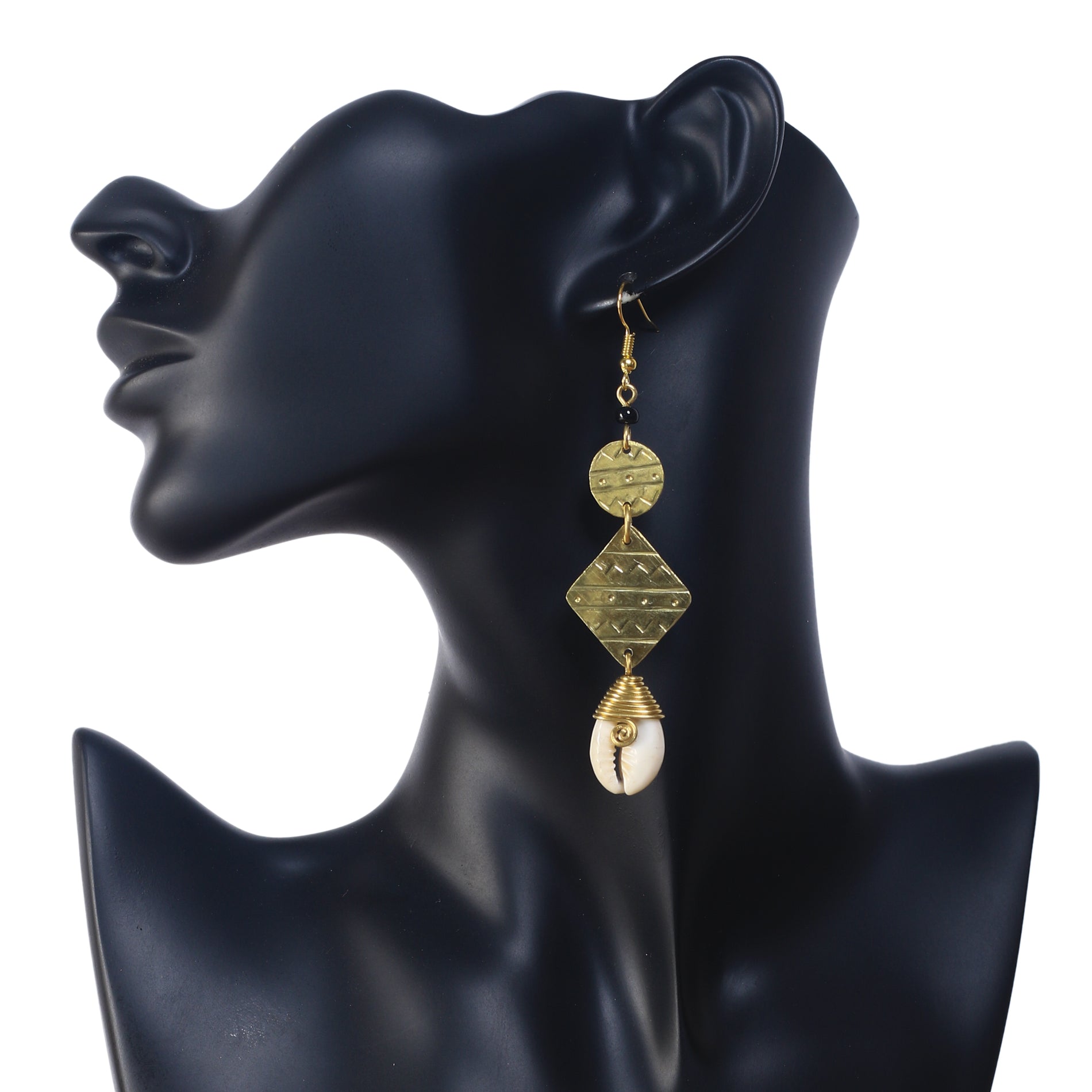 Long gold dangle earrings featuring a black bead, etched geometric shapes, and a wire-wrapped cowrie shell at the bottom.