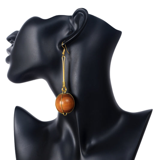 A pair of long, gold-plated bar dangle earrings with a large wooden sphere in a gold wire cage at the bottom.