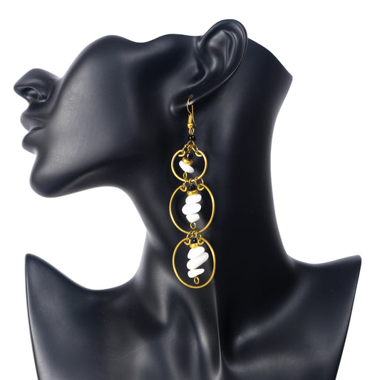 Long gold-plated earrings with three stacked rings, each holding a central dangle of white stone chips and black beads.