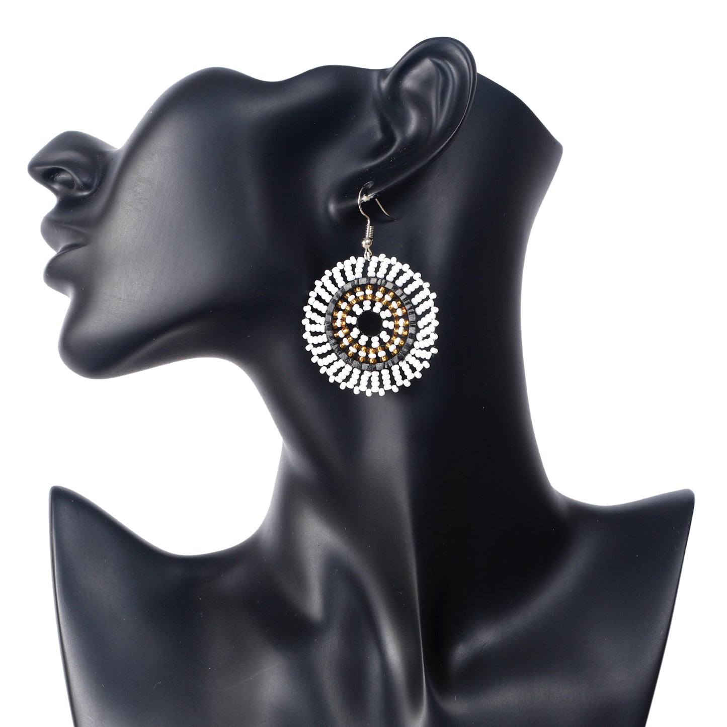 A pair of hand-woven white, gold, black, and silver beaded disc earrings in a concentric circle pattern.