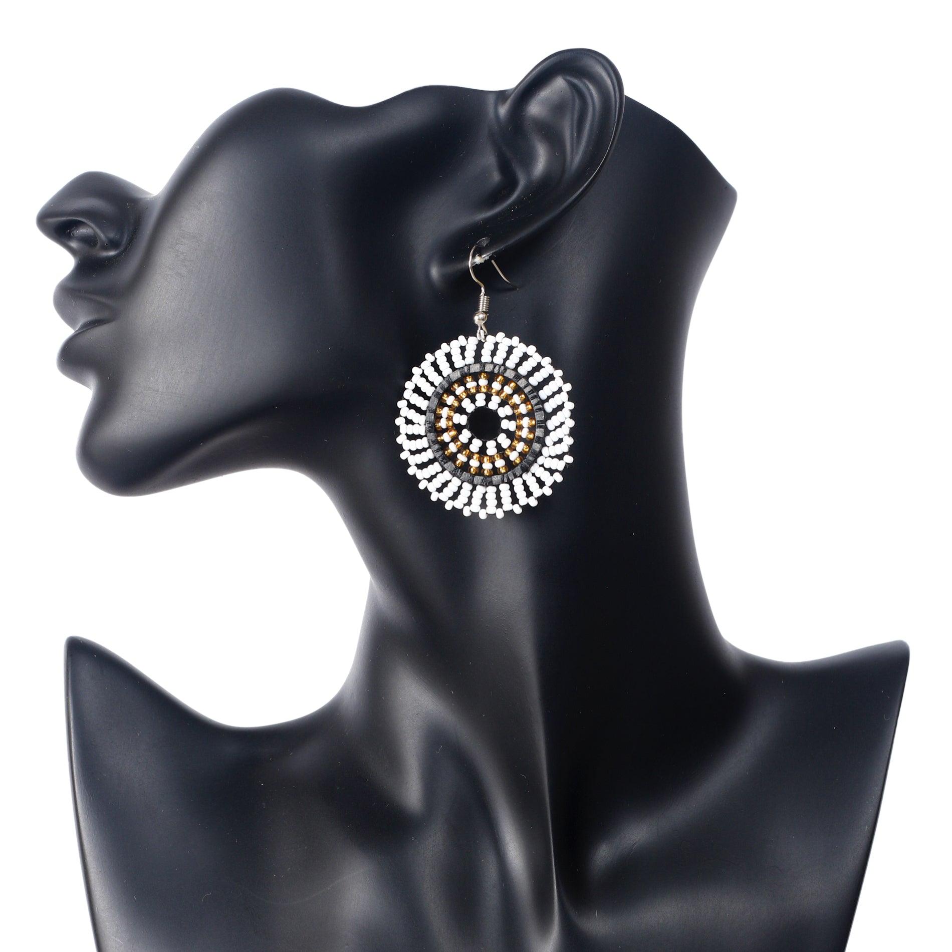 A pair of hand-woven white, gold, black, and silver beaded disc earrings in a concentric circle pattern.